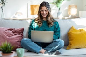 Beautiful kind woman working with laptop while sitting on couch in living room at home