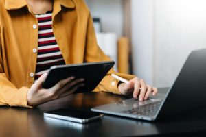 Hands of woman using mobile phone in modern office with laptop and digital tablet at home office